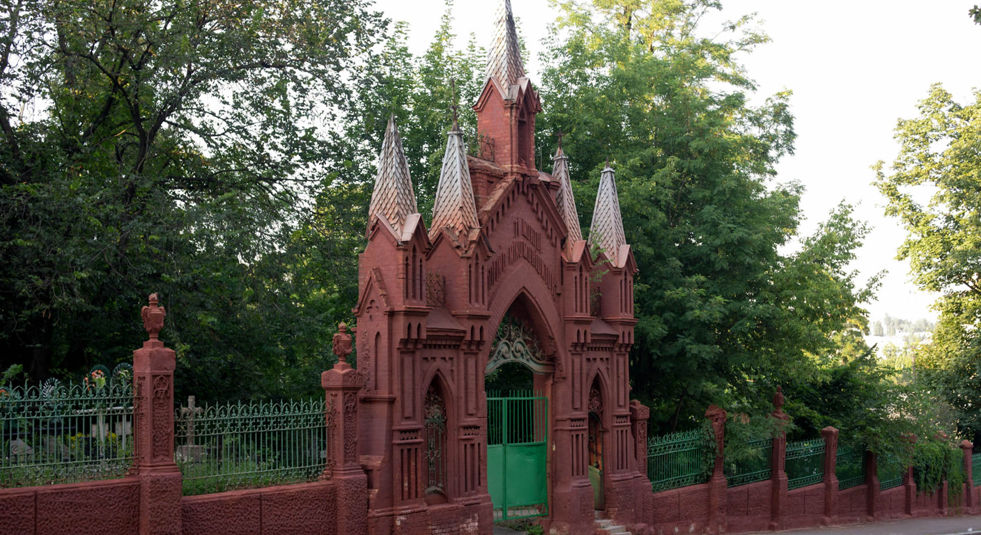 Ornate cemetery gates beneath a canopy of trees in soft daylight