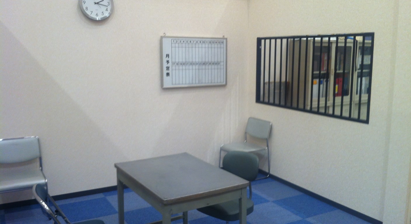 A stark police interrogation room with a table, empty chairs, and a viewing window